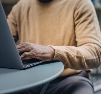 crop trendy african american man using laptop in street cafe