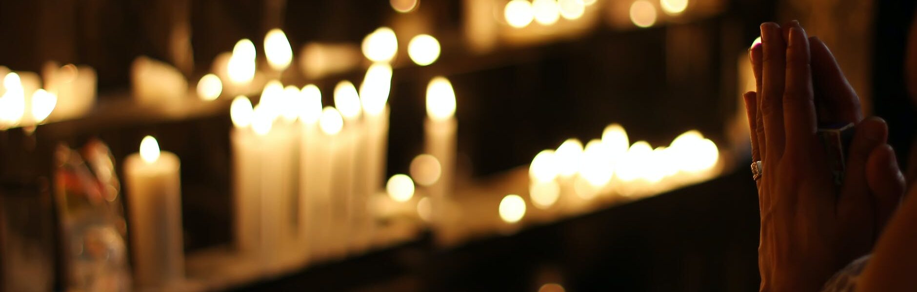 close up photograph of person praying in front lined candles